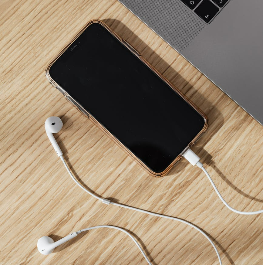 a smartphone sits on a wood table next to a laptop keyboard with headphones plugged in.