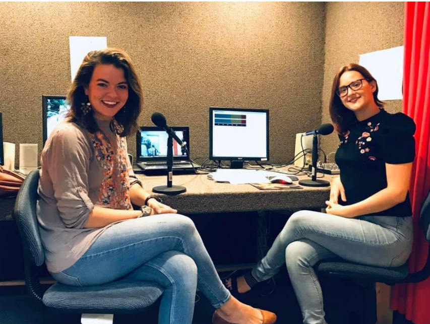 Alex sits in an audio studio with a woman, both sitting and smiling.